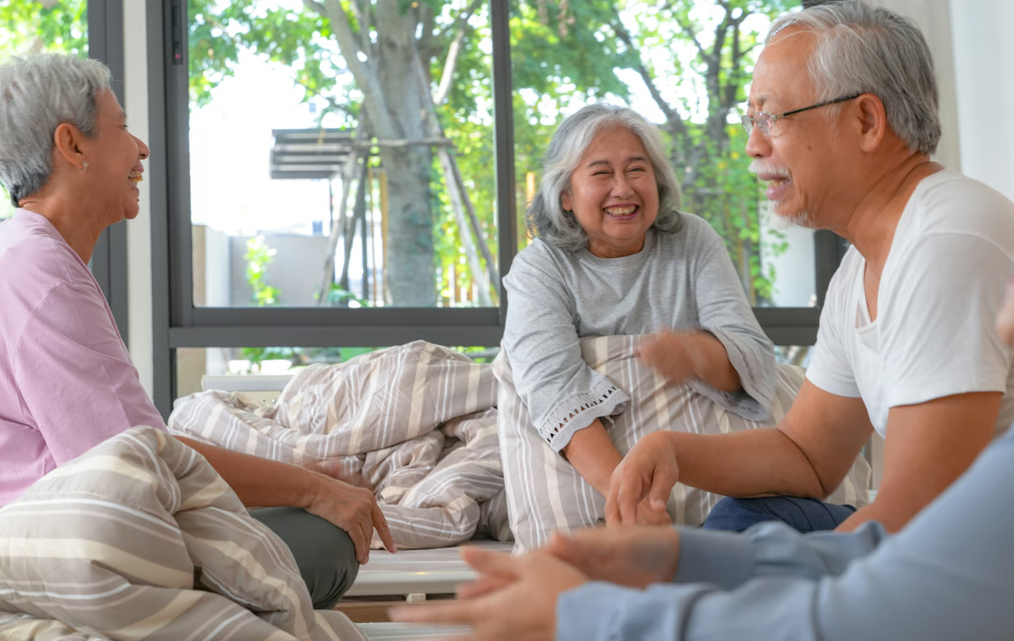 A happy senior patient laughing with family members while relaxing comfortably on a bed during home-based hospice care.